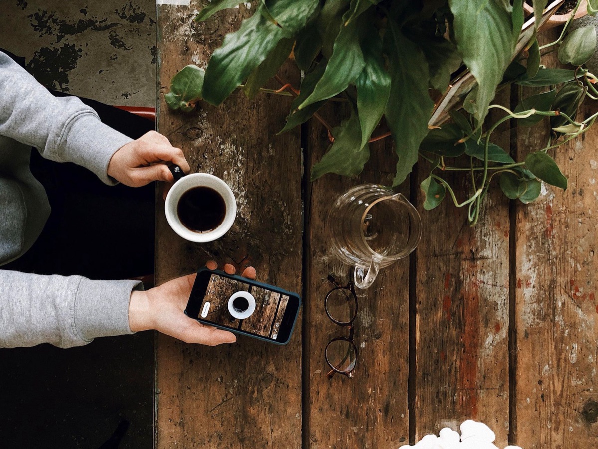 Person mit Kaffeetasse und Smartphone