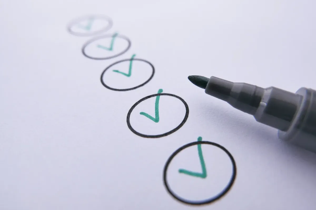 Close-up of a checklist with green checkmarks on white paper using a marker.