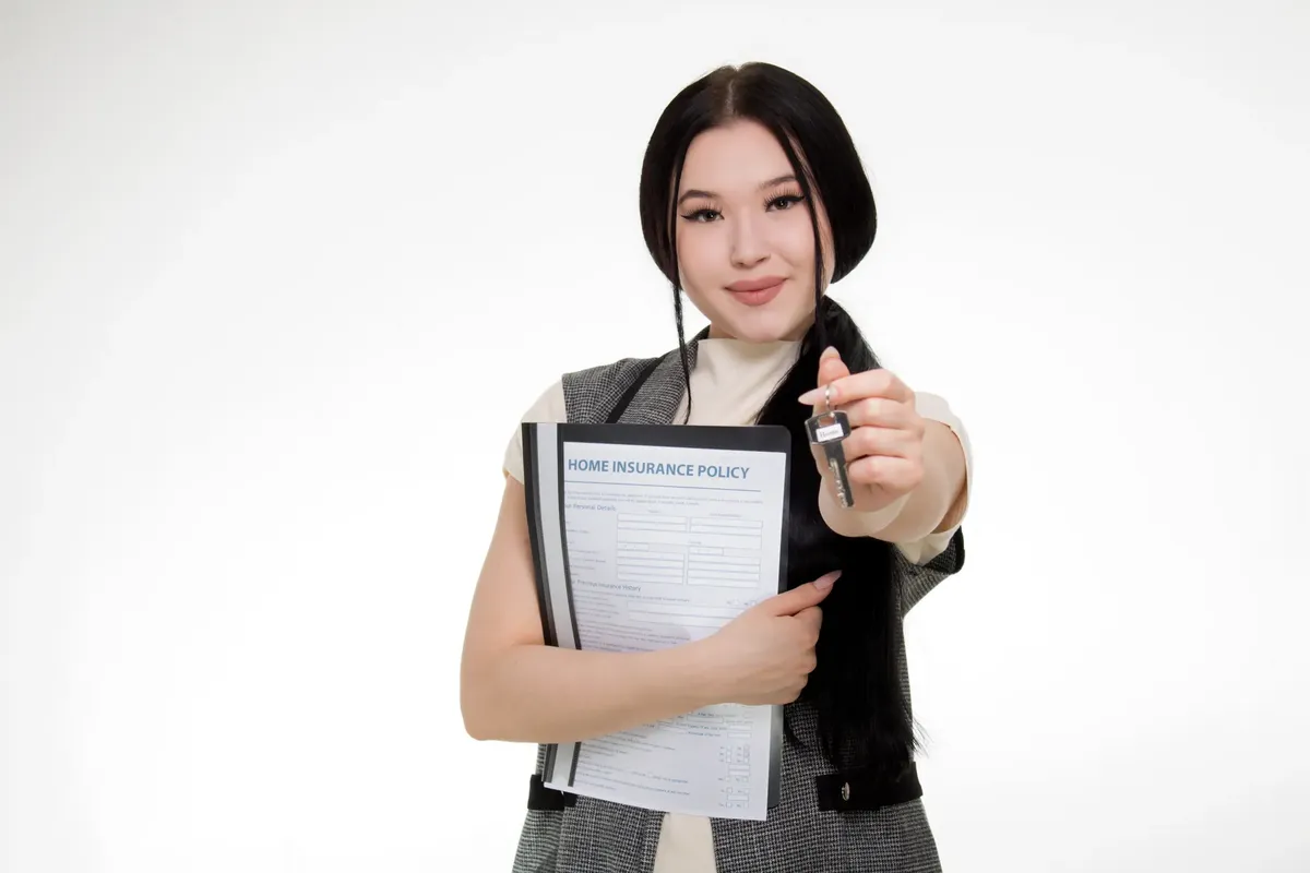 Asian woman smiling while holding a home insurance policy and a key, symbolizing new home ownership.