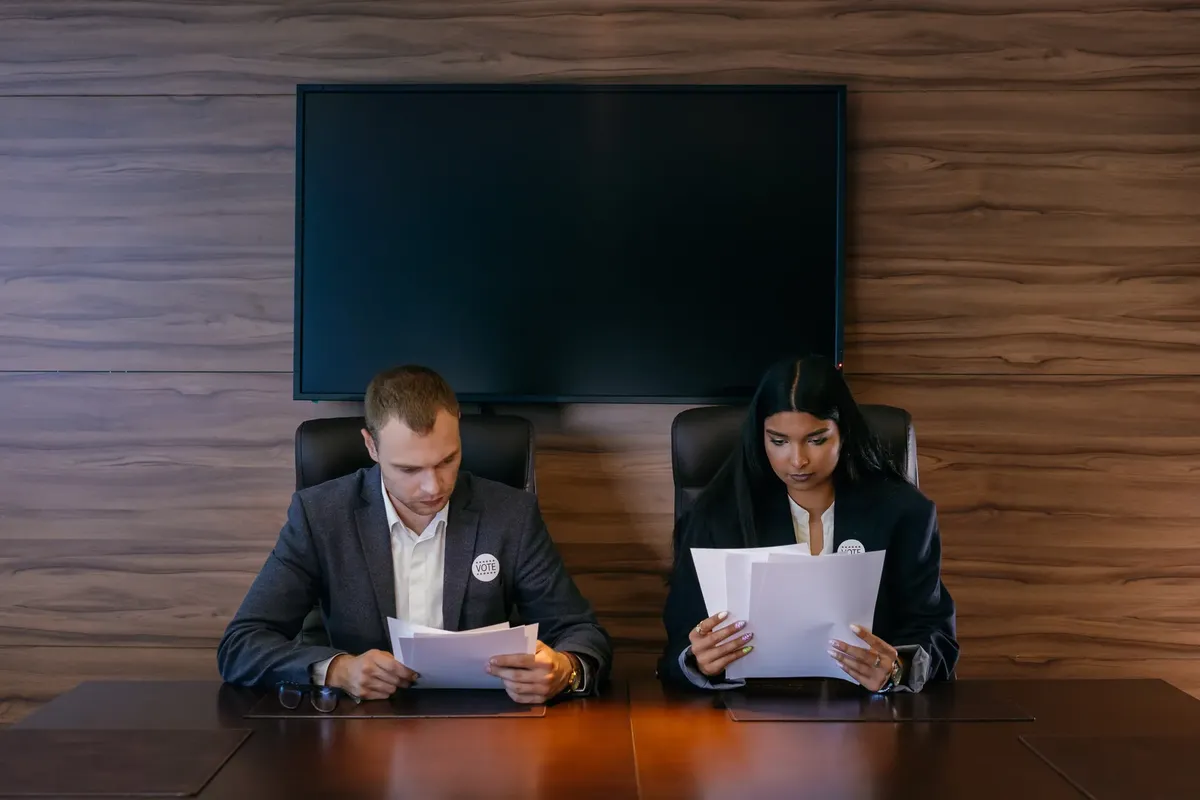 Two professionals reviewing documents at a meeting table in a modern conference room.