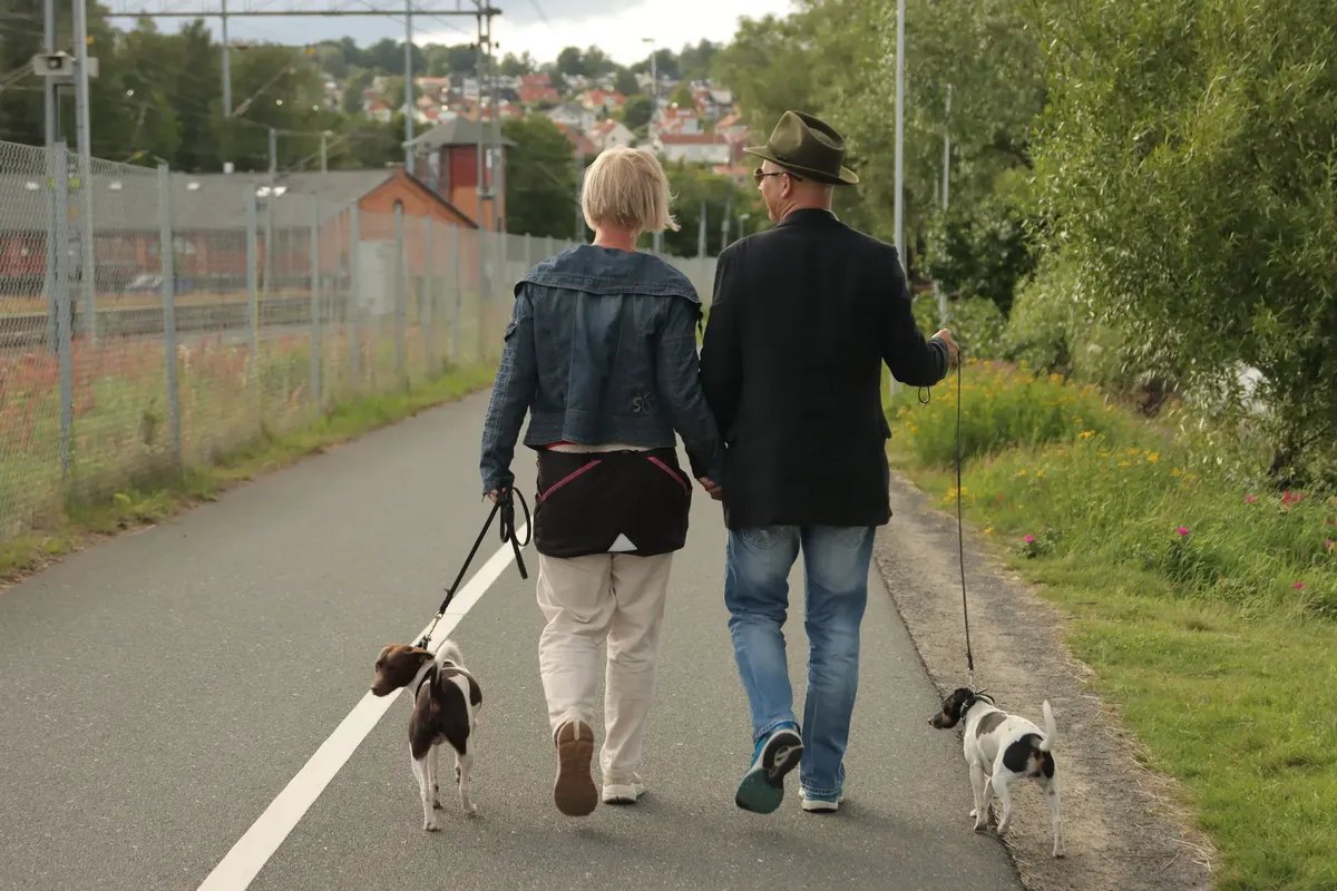 A couple walking their dogs on a scenic path in Jönköping, Sweden, showcasing an outdoor lifestyle.