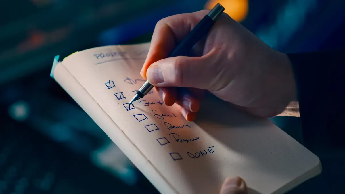 Close-up of a hand writing a checklist in a notebook, symbolizing productivity and organization.