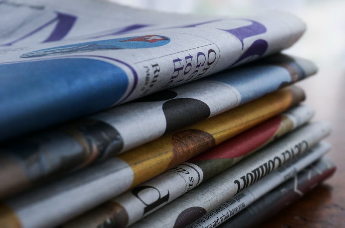 Zeitungsartikel und Versicherungspolice auf einem Tisch.